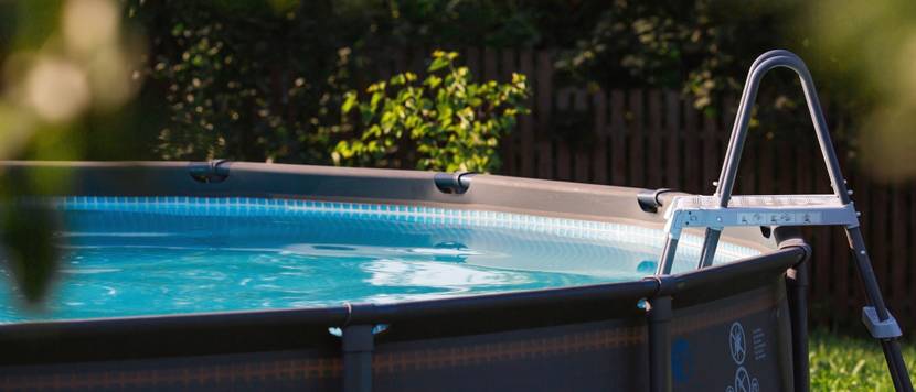 Ein grauer Aufstellpool mit Leiter steht in einem Garten.