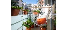Sommerlicher Stadtbalkon mit verschiedenen Pflanzen und einem Hängesessel.