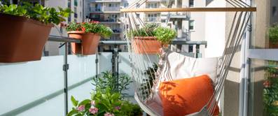 Sommerlicher Stadtbalkon mit verschiedenen Pflanzen und einem Hängesessel.