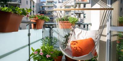 Sommerlicher Stadtbalkon mit verschiedenen Pflanzen und einem Hängesessel.