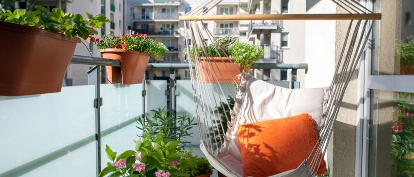 Sommerlicher Stadtbalkon mit verschiedenen Pflanzen und einem Hängesessel.