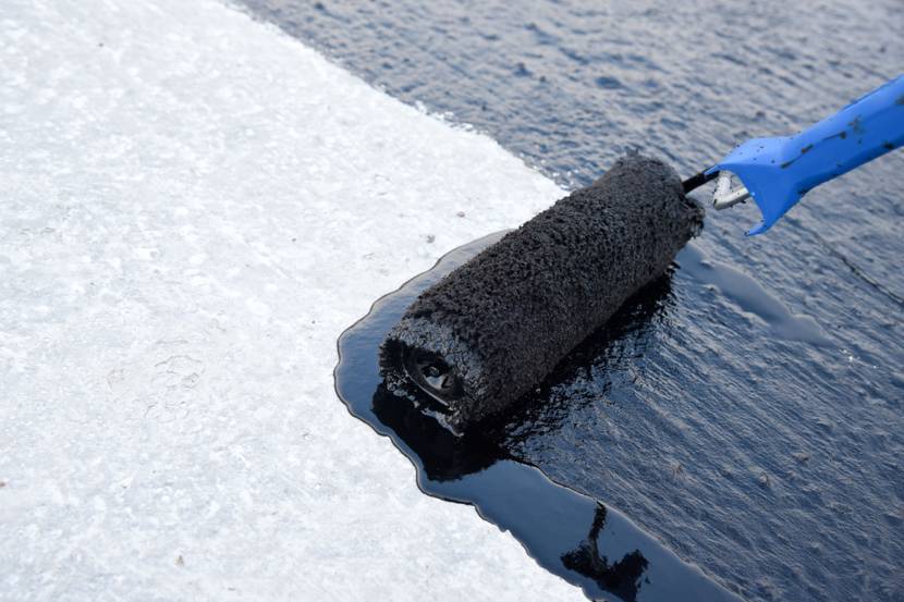 Bitumen wird mit einer Rolle auf einem Kellerboden verteilt.