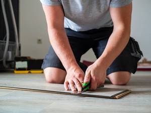 Junger Mann mit Cuttermesser in der Hand beim Bodenverlegen
