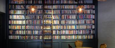 Volles Bücherregal mit Leiter vor einer hohen Wand.