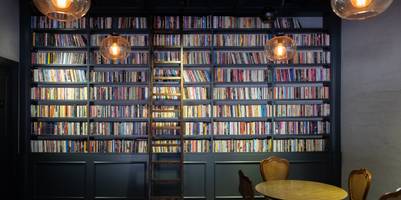 Volles Bücherregal mit Leiter vor einer hohen Wand.