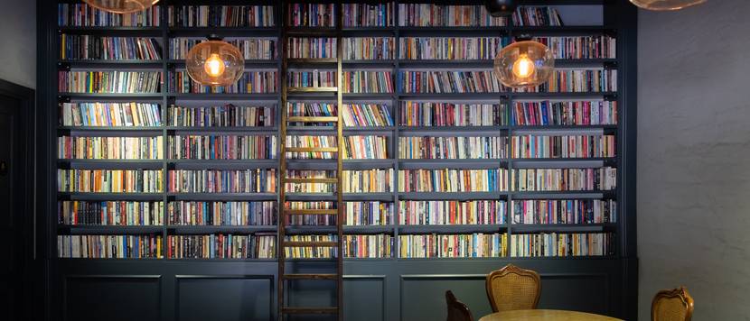 Volles Bücherregal mit Leiter vor einer hohen Wand.