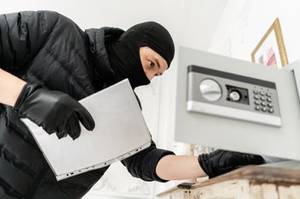 Maskierter Einbrecher nimnt Dinge aus Safe