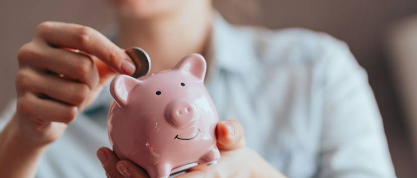 Eine Frau hält ein Sparschwein in der Hand, in das sie eine Münze steckt.
