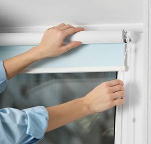 person bringt rollos an fenster an