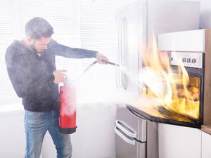 Mann löscht Feuer im Ofen mit dem Feuerlöscher in der Küche