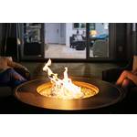 Auf einer Terrasse vor einem Haus brennt in einer Feuerschale ein Feuer. Zu beiden Seiten befinden sich Beine von sitzenden Personen.