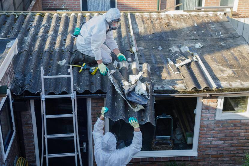 zwei Personen in Schutzanzügen entfernen asbestbelastete Dachabdeckungen