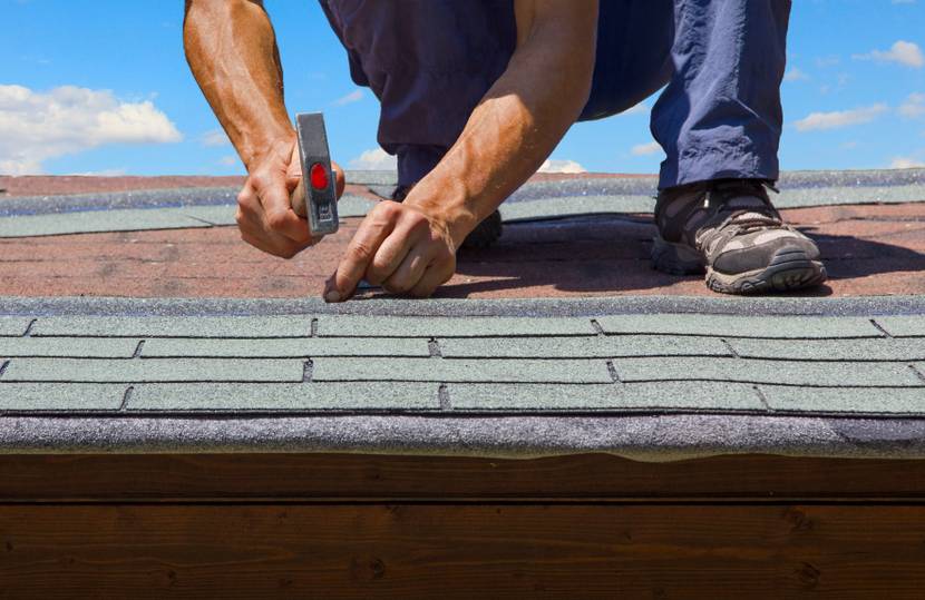 Person erneuert ein Dach mit gemusterter Dachpappe, zu sehen sind Hände, die einen Hammer nutzen