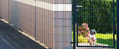 Doppelstabmattenzaun am Rand eines Gartens eines Hauses, davor Bürgersteig.