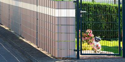 Doppelstabmattenzaun am Rand eines Gartens eines Hauses, davor Bürgersteig.