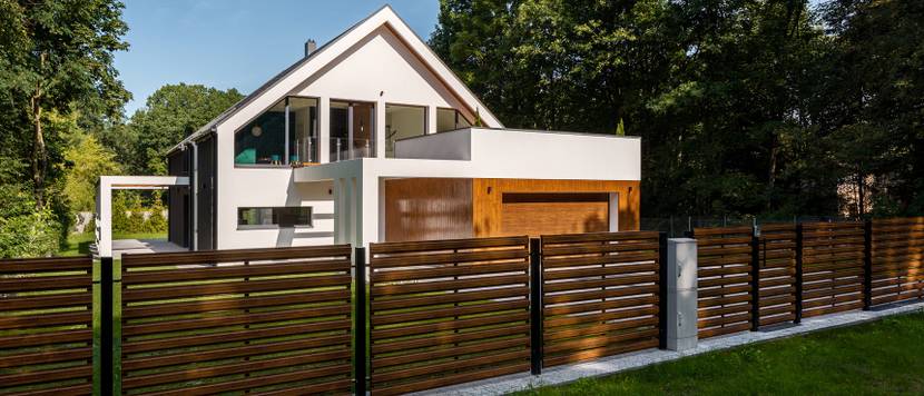 Zaun mit Metallgerüst und Holzlatten vor einem modernen Haus.