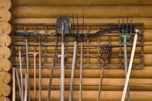 Gartengeräte stehen vor einer Holzwand nebeneinander aufgereiht.
