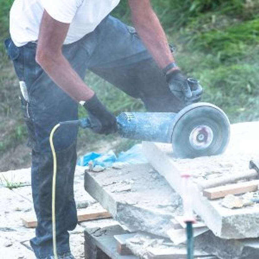 Bauarbeiter schneidet Steinblock mit Winkelschleifer.