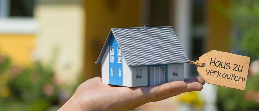 Haus verkaufen: Eine Person hält ein Modellhaus mit einem Schild mit der Aufschrift 