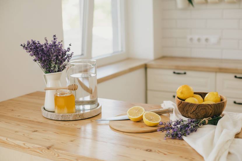 Auf einer Kücheninsel stehen eine Schale mit Zitronen, ein Schneidebrett mit einer aufgeschnittenen Zitrone sowie eine Vase mit Lavendel, Honig und eine Wasserkaraffe.
