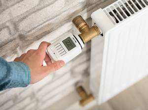 Person stellt elektrisches Thermostat ein