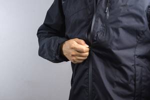 Herren-Regenjacke im Test: Schwarze Herren-Regenjacke wird am Reißverschluss zugezogen.