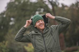 Herren-Regenjacke im Test: Fröhlicher Mann zieht die Kapuze der Regenjacke über.