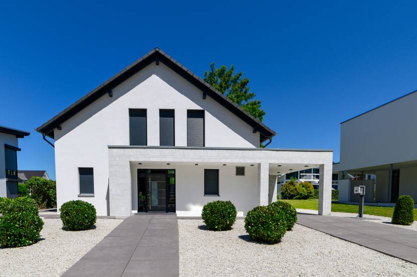 Modernes weißes Haus mit Vorgarten aus Steinbeeten und Buchsbäumen im Sommer.