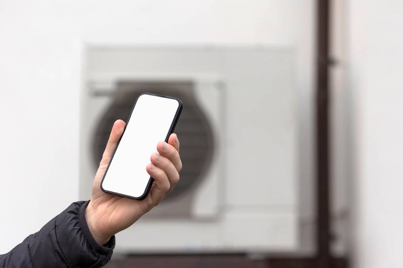 Hand mit Smartphone vor Wärmepumpenhintergrund zur Steuerung von Betriebszeit und Temperatur.
