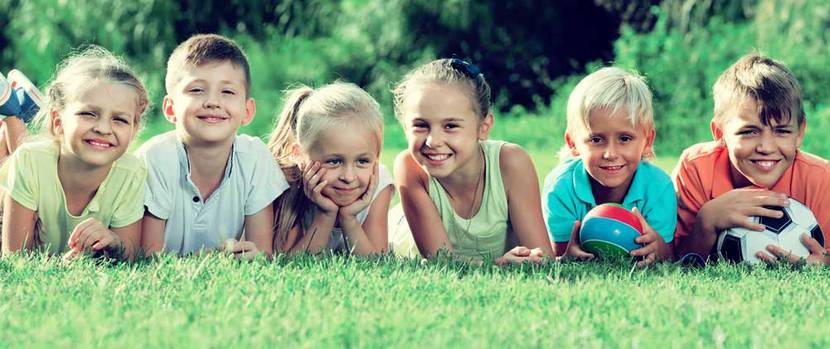 Sechs Kinder liegen mit zwei Bällen im Garten auf dem Bauch.