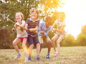 Multikulturelle Gruppe Kinder beim Tauziehen als Team in der Natur