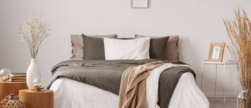 Bett mit Kissen und Decken in Brauntönen in einem modern eingerichteten Schlafzimmer.