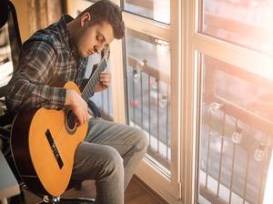 Mann spielt Gitarre vor Fenster