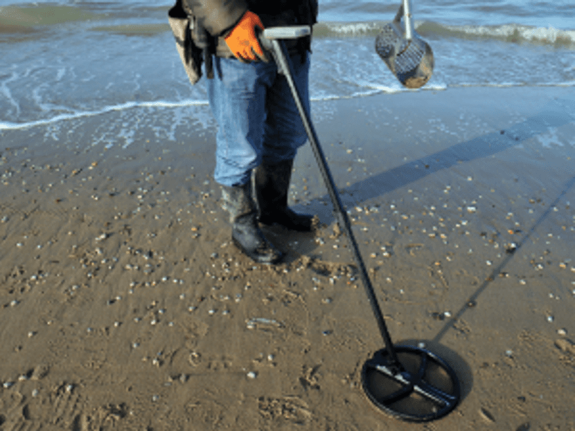 Mensch sucht mit Metalldetektor am Strand