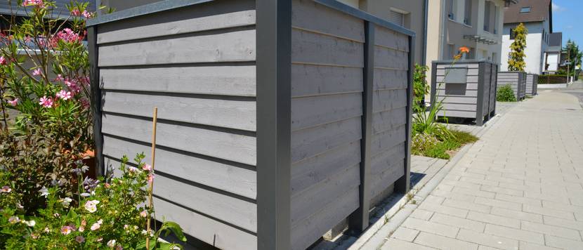 Vor Reihenhäusern stehen Mülltonnenboxen, die mit grau gefärbtem Holz verkleidet sind.