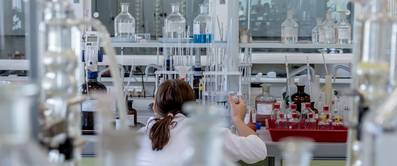 Must Have Laborarbeit: Chemikerin von hinten beim Arbeiten im Labor zu sehen.