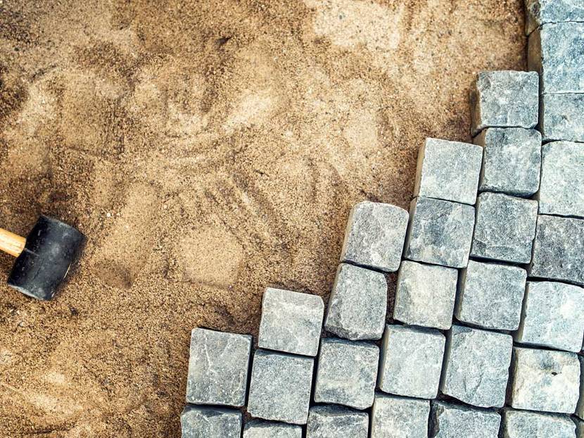 Mit dem Pflasterhammer werden die Pflastersteine in den Sand gesetzt.
