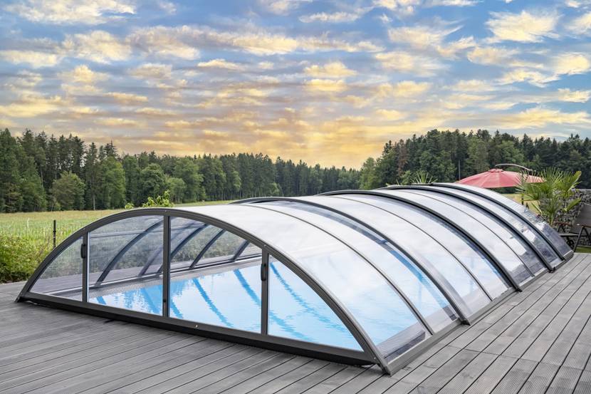 Eine halbhohe Poolüberdachung über einem Pool. Im Hintergrund ist ein Wald zu sehen.