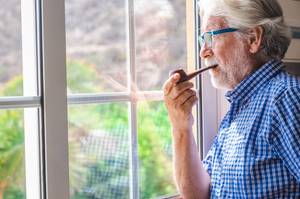 älterer mann steht am fenster und raucht pfeife