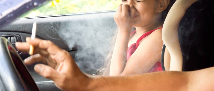 kind hält sich im auto die nase zu während der vater zigarette raucht