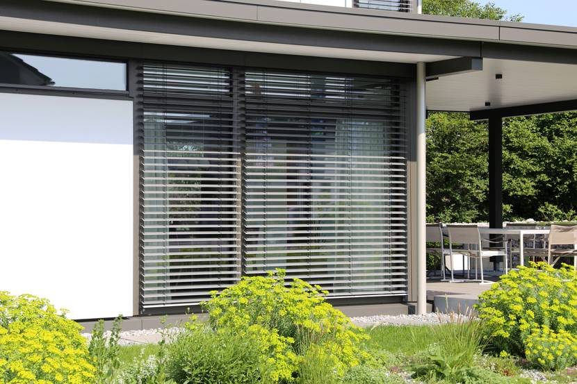 Die Fenster eines weißen Hauses werden durch Rollläden verdunkelt.