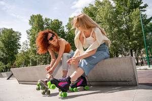 Rollschuhe getestet: zwei Frauen mit Rollschuhen sitzen lächelnd auf einer Mauer.