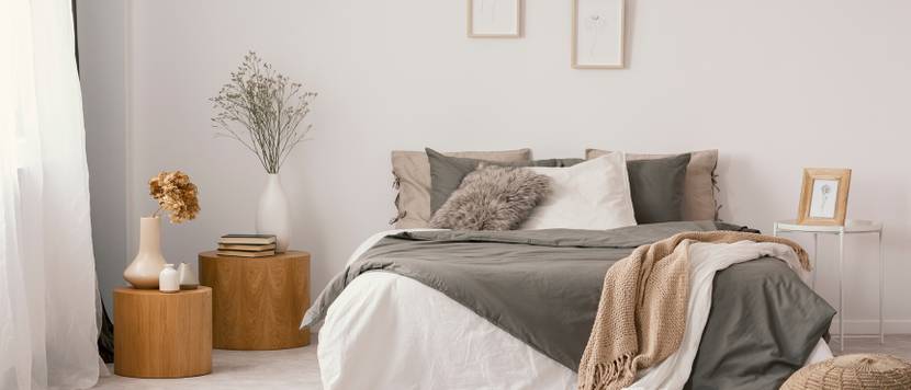 Schlafqualität verbessern durch ein passendes Bett im Test: Bett mit Decken und Kissen, zwei Bildern über dem Bett und Dekoelementen neben dem Bett.