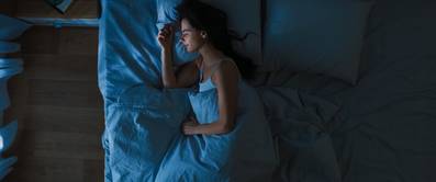 Schlafqualität verbessern durch Dunkelheit im Test: Frau liegt in Dunkelheit in einem Bett und schläft.