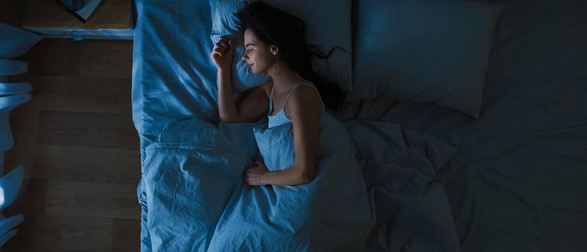 Schlafqualität verbessern im Test durch Dunkelheit: Frau liegt in Dunkelheit in einem Bett und schläft.