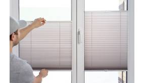 Ein Mann bringt Plissees an einem Fenster in Position.