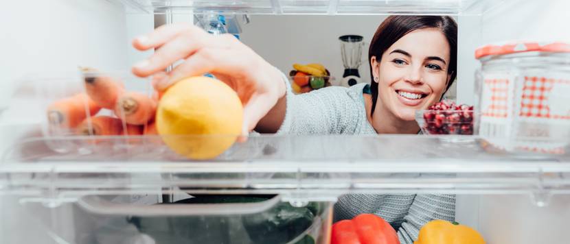 Frau greift nach Obst im Kühlschrank