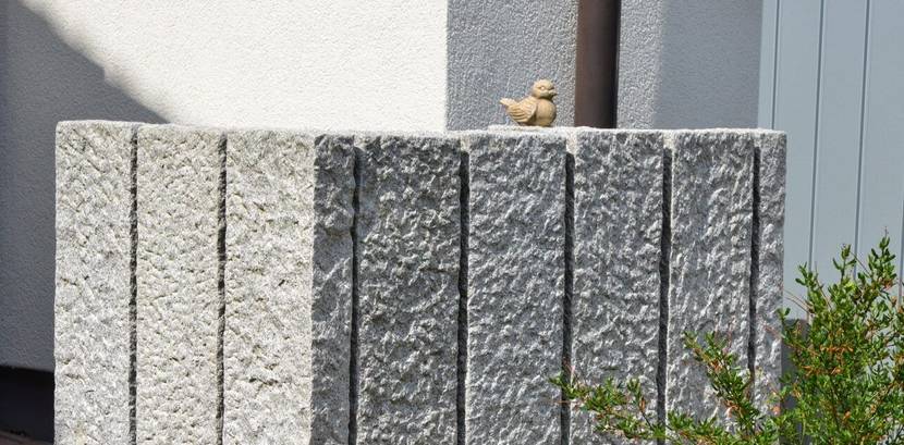 Sichtschutz-Mauer aus rohen Granitsäulen um Abfallsammelbehälter