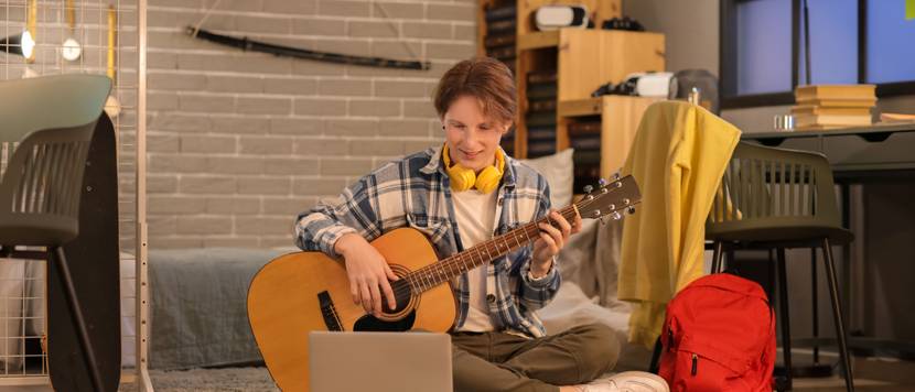 Teenager spielt Gitarre, während er auf einem hellgrünen Teppich sitzt.