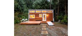 Tiny House in der Dämmerung vor einem Wald.